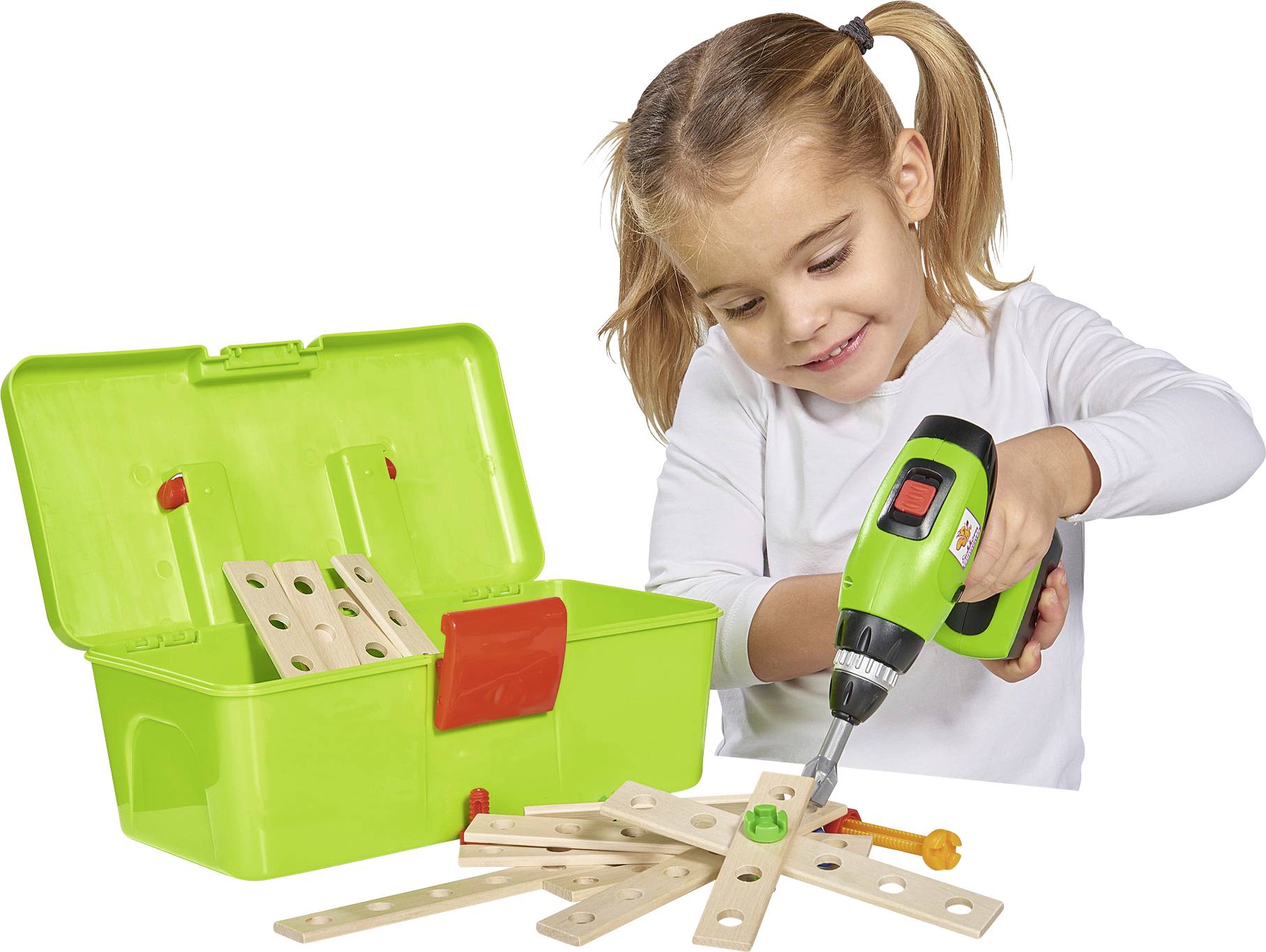 A girl is using a green, battery-powered toy drill to assemble a wooden toy. A green toolbox is standing nearby.