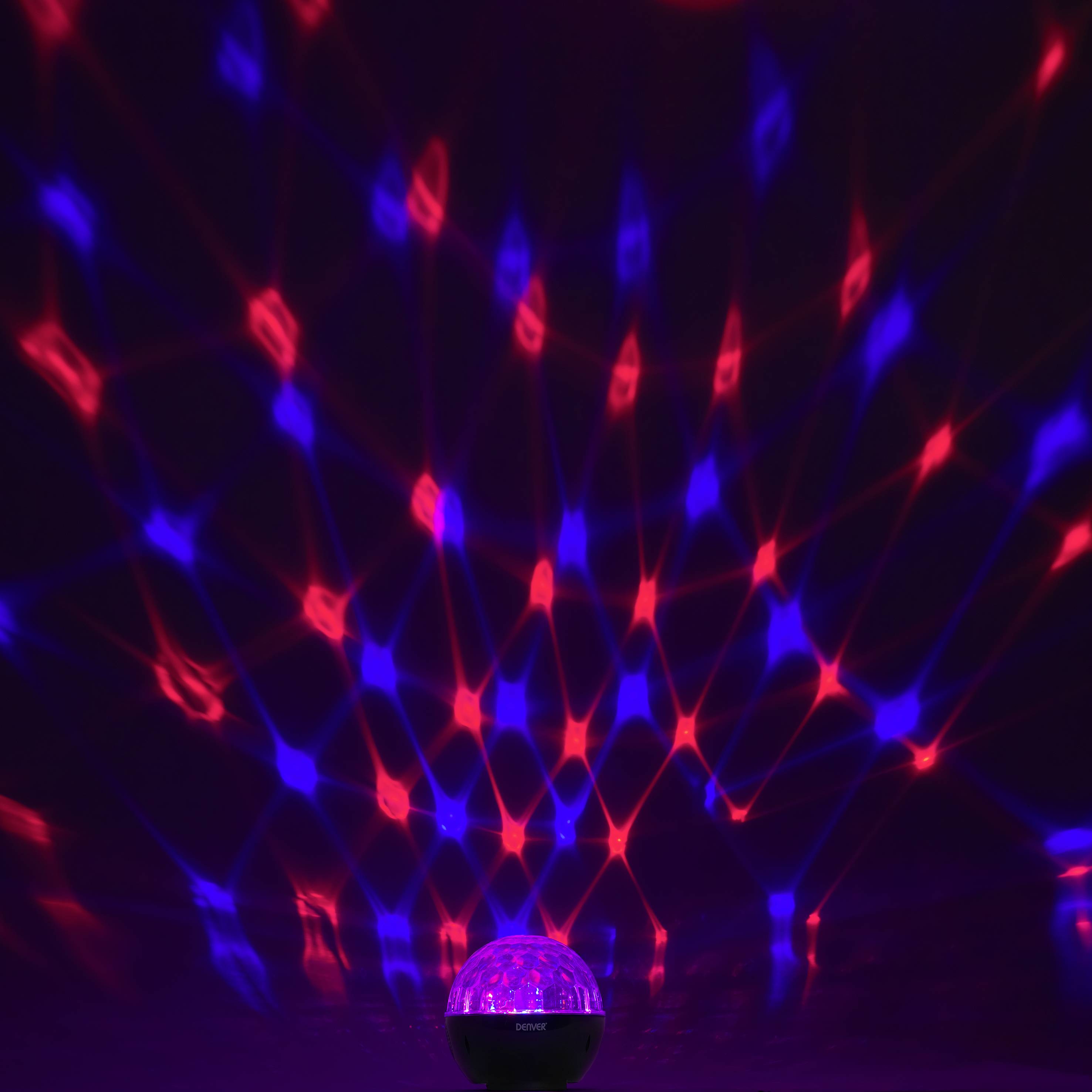 A glowing spherical lamp projects red and blue lights in a grid pattern onto the walls of a dark room.
