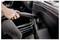 A person vacuuming the interior of a car, focusing on a crevice between the seat and dashboard, using a handheld vacuum cleaner.
