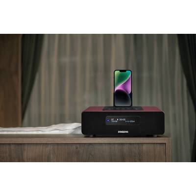 A smartphone sits on a red soundbox on a wooden table, with dark curtains visible in the background.