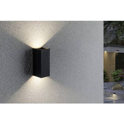 A modern exterior light with a black housing emits light upwards and downwards along a textured grey wall.
