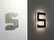 The letter 'S' is mounted on a wall, on the left in white with a shadow, on the right in black with a backlit glow.