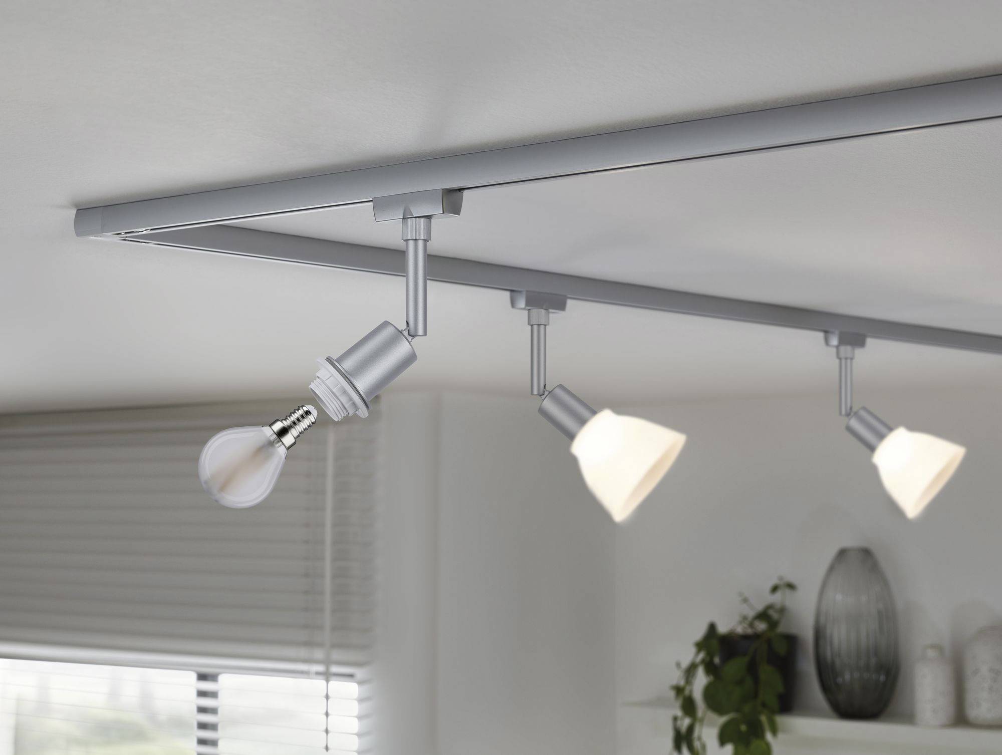 Three adjustable ceiling lights, two with lampshades illuminating, one without a shade. Modern living room lighting.