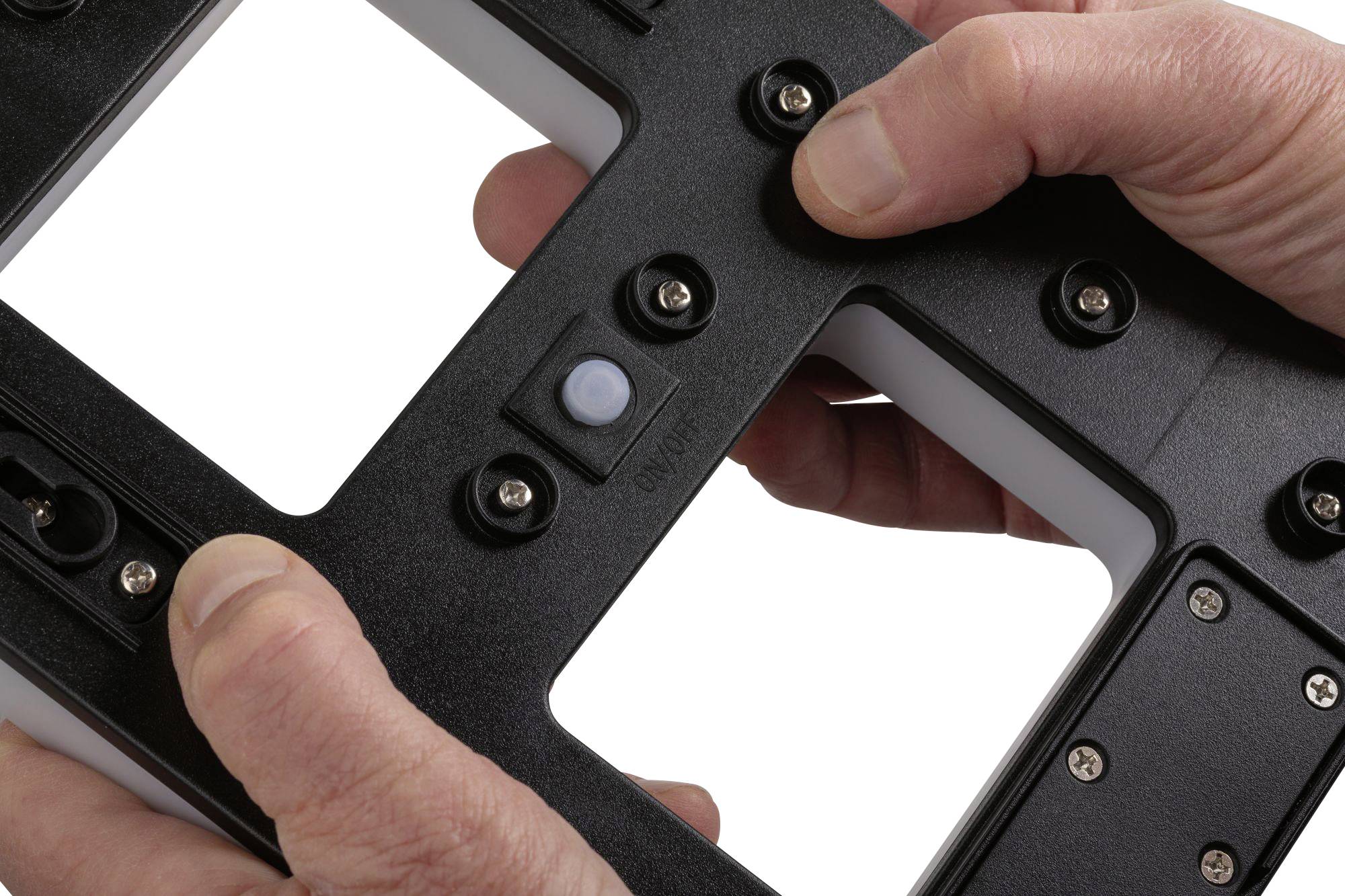Two hands are holding a black frame with attached screws and a small sensor in the centre.