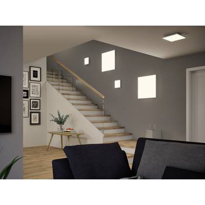 Staircase in a modern living space with wooden flooring; white staircase, grey wall with pictures, plants on a table and lighting on.