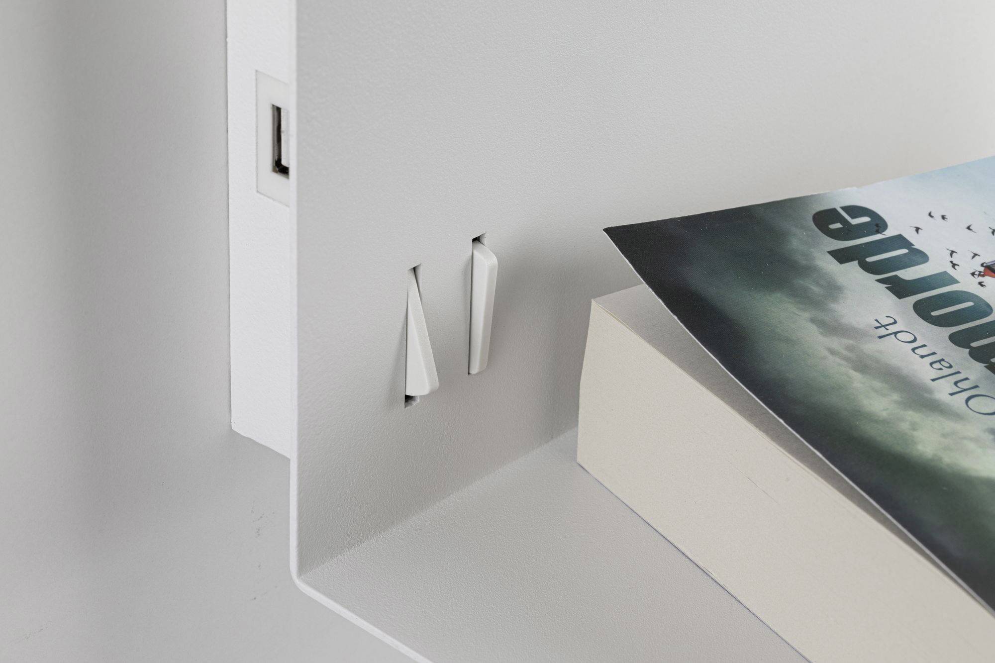 A shelf with a book 'Lost Honour' and two plug sockets. Modern, minimalist furnishings.