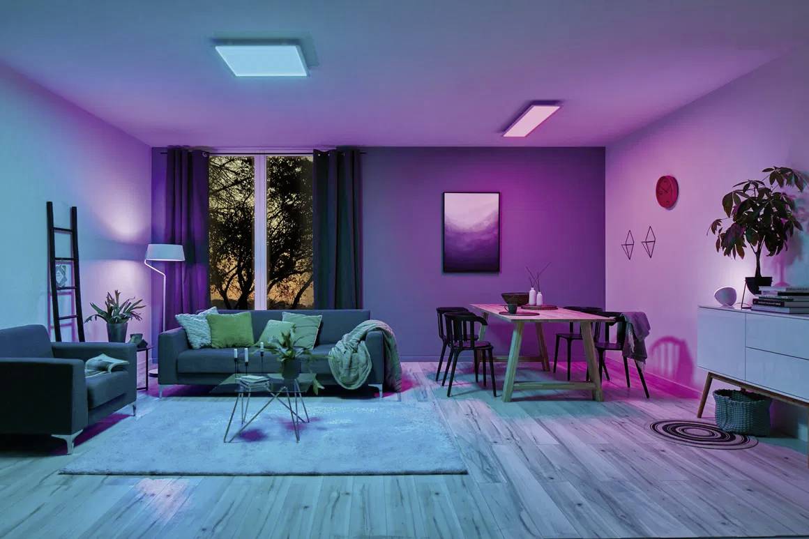 Living room with colourful lighting. Sofa, table, chairs and plants. Window with a view of the sunset. Modern decoration.