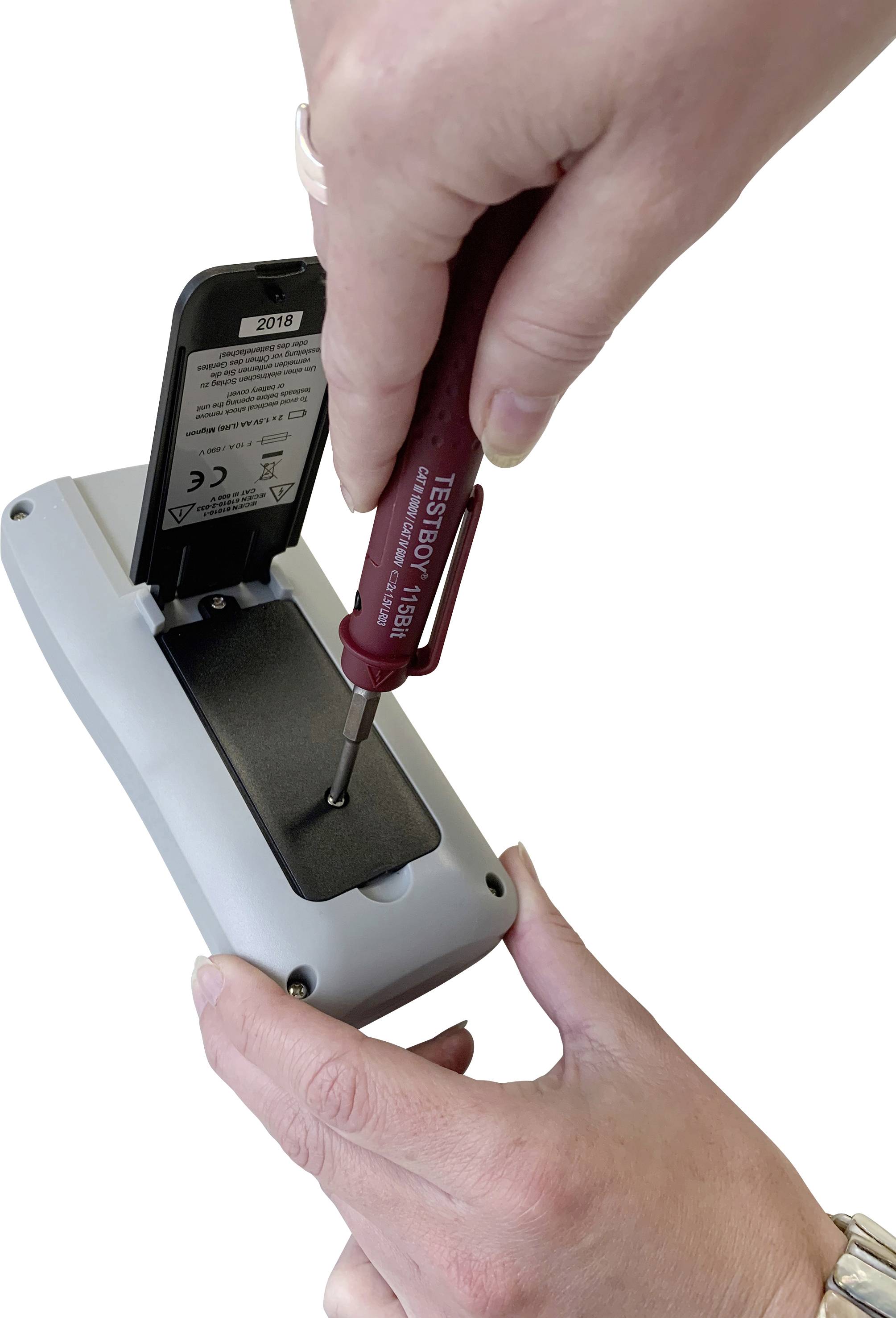 A person is holding a screwdriver and opening the cover of an electronic device to expose the battery compartment.