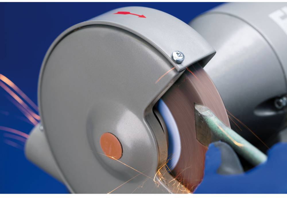 A metal part is being sharpened by a grinding machine with sparks flying. Protective equipment is visible.