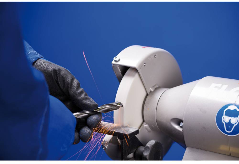 A person is grinding a metal drill bit on a bench grinder. Sparks are flying as the drill bit is being sharpened.