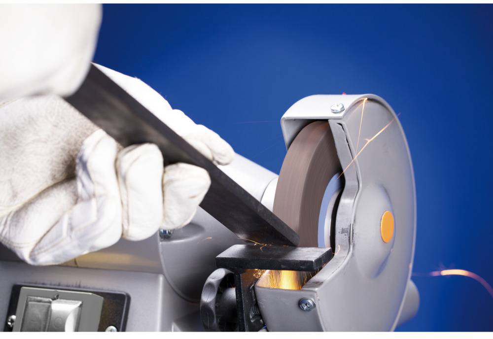 A metal rod is being machined with a grinding wheel. Sparks fly as the rod is pressed against the rotating wheel.