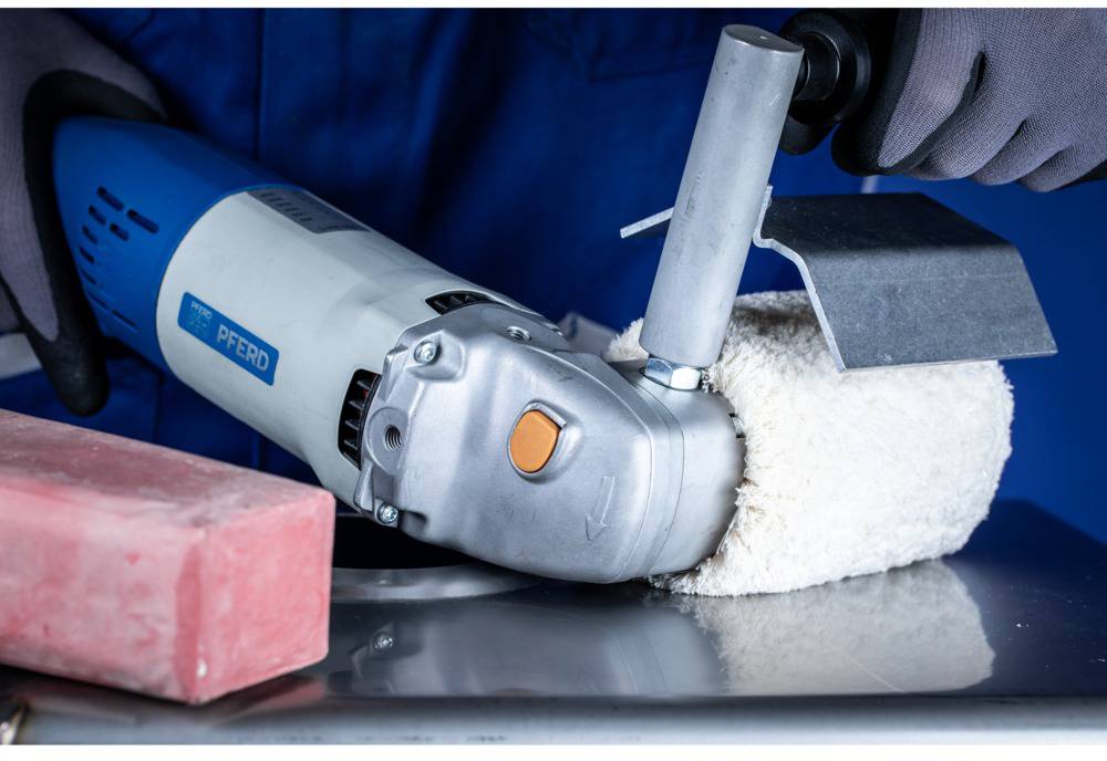 A person is working on a metallic surface with an electric tool and a polishing attachment. In the foreground, a red block and protective clothing can be seen.