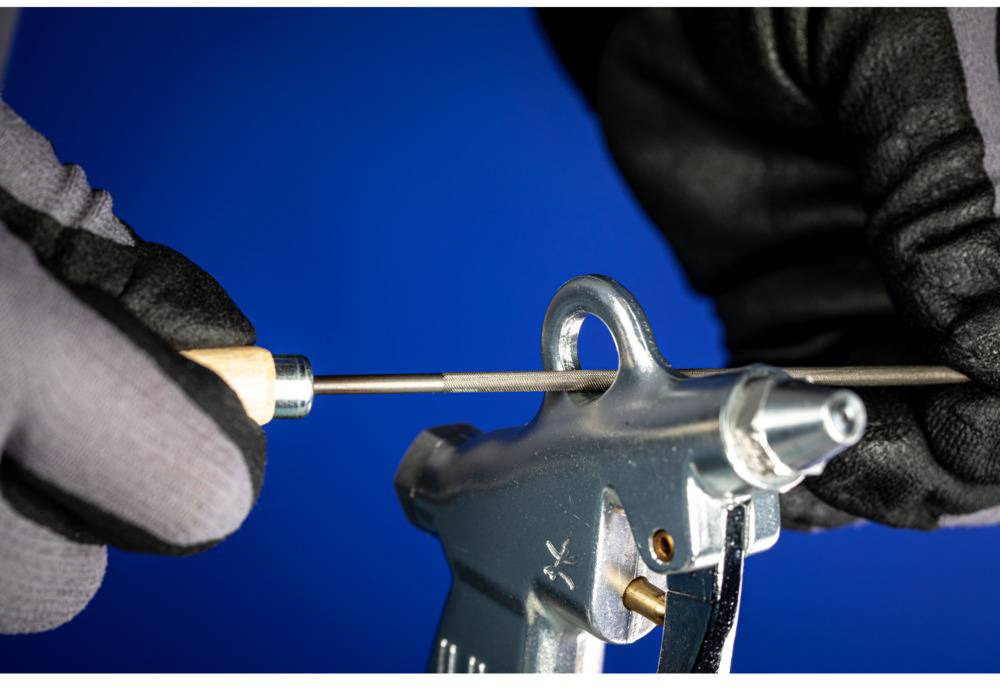 Two gloved hands hold and work with a silver tool using a file against a blue background.