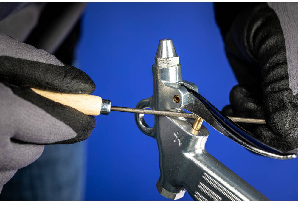 A person wearing gloves is holding a metal tool and inserting a rod into the barrel, presumably for cleaning or maintaining a piece of equipment.