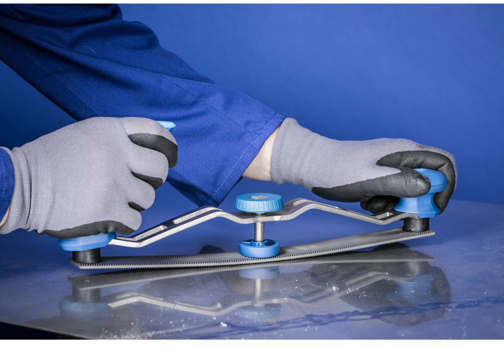 'A person in work attire and gloves is moving a manual tool over a metal sheet to smooth the surface.'