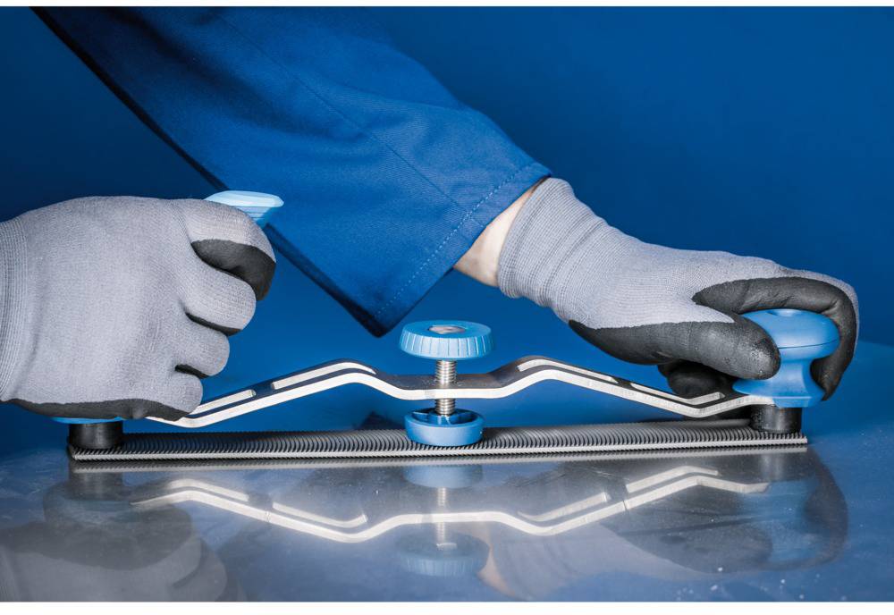 A person in blue workwear is using a hand tool for metalworking. The tool has blue handles and glides across a metal surface.