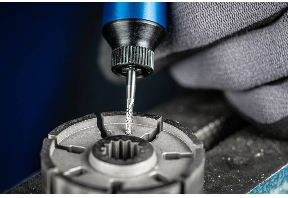 A gloved hand holds a precision tool being inserted into a metal mount, illustrating a machining process.