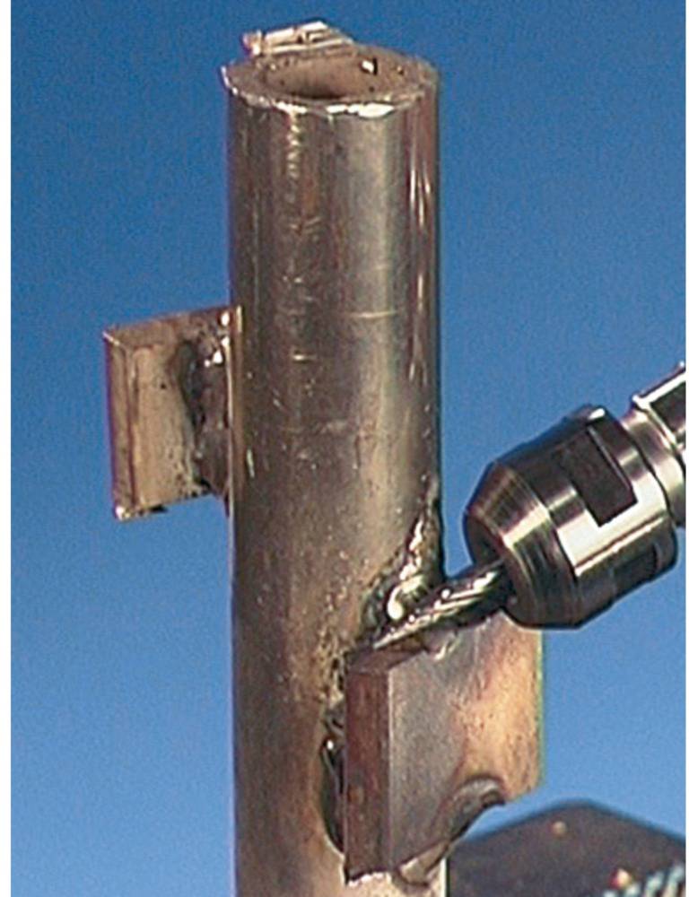 'Metal drill working on vertical pipe, creating a hole. Metal construction process in action.'