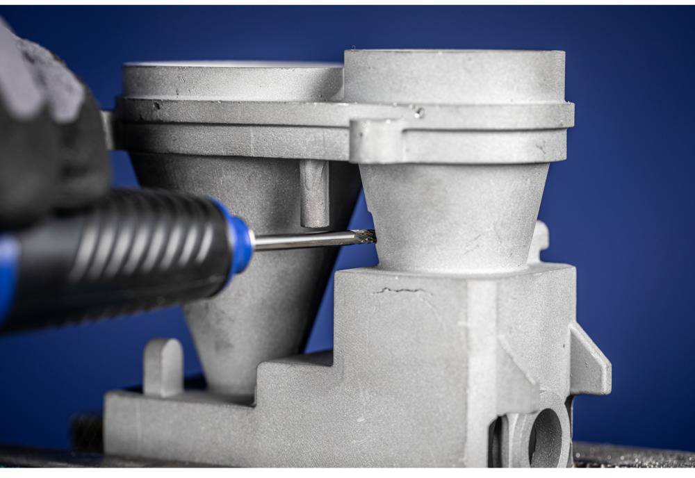 'Close-up of a metal die-cast component being machined with a tool. The focus is on the precision of the work.'