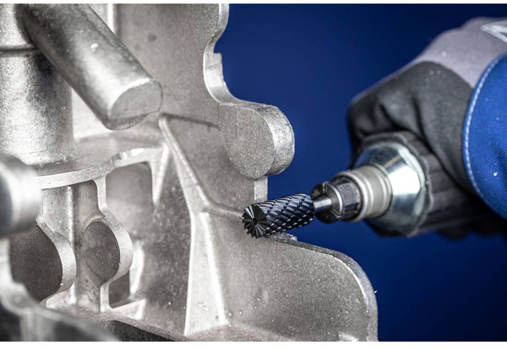 A close-up of a worker wearing protective clothing and machining metal with a grinding tool.