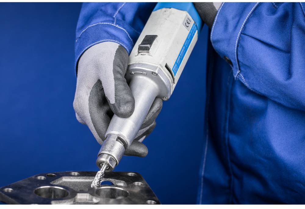 'Person in blue workwear using an electric tool to drill holes in a metal plate.'