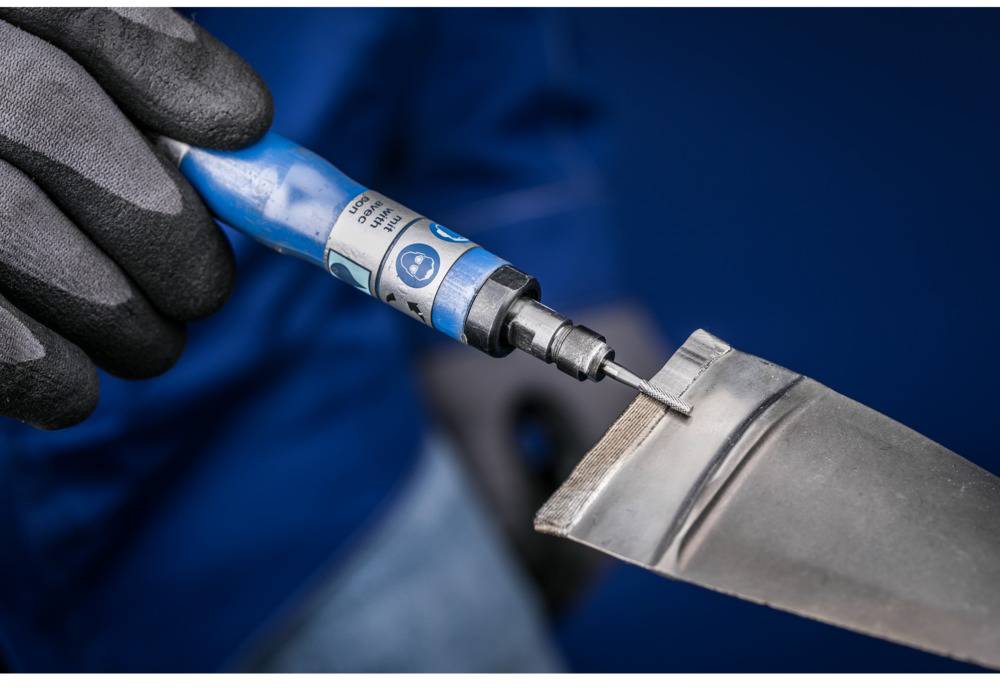 Close-up of a person wearing a black glove using a blue electric tool to edge a piece of metal.