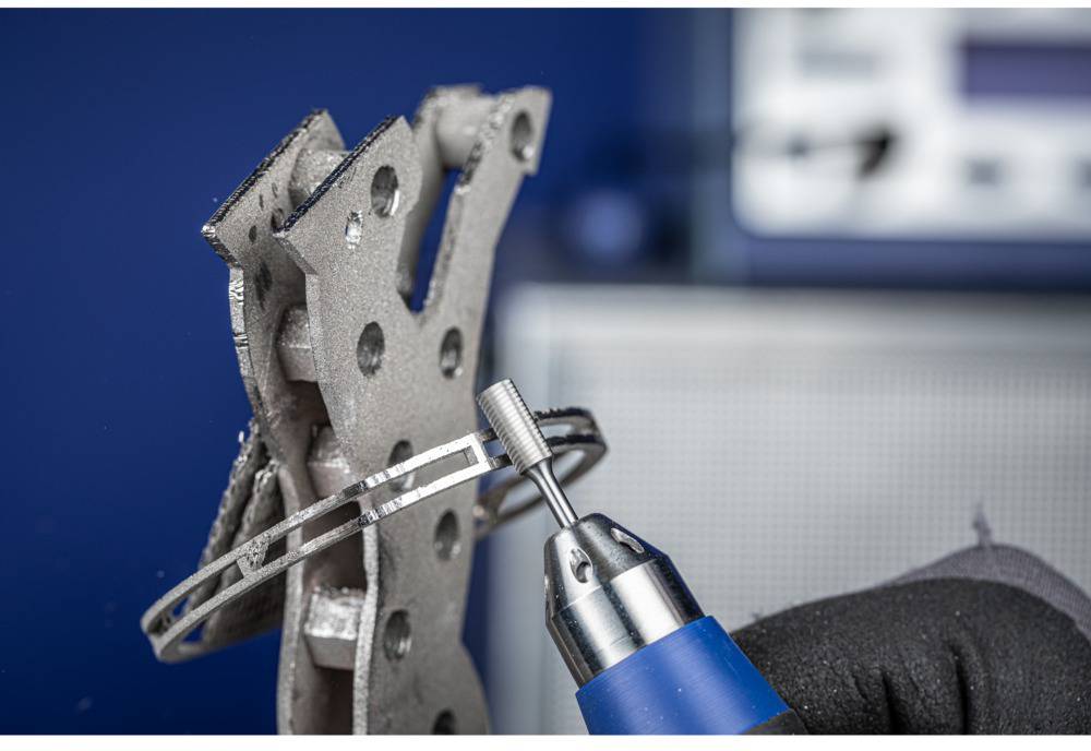A metal plate is being machined with a rotating tool. The plate has several holes, and the tool is blue and silver.