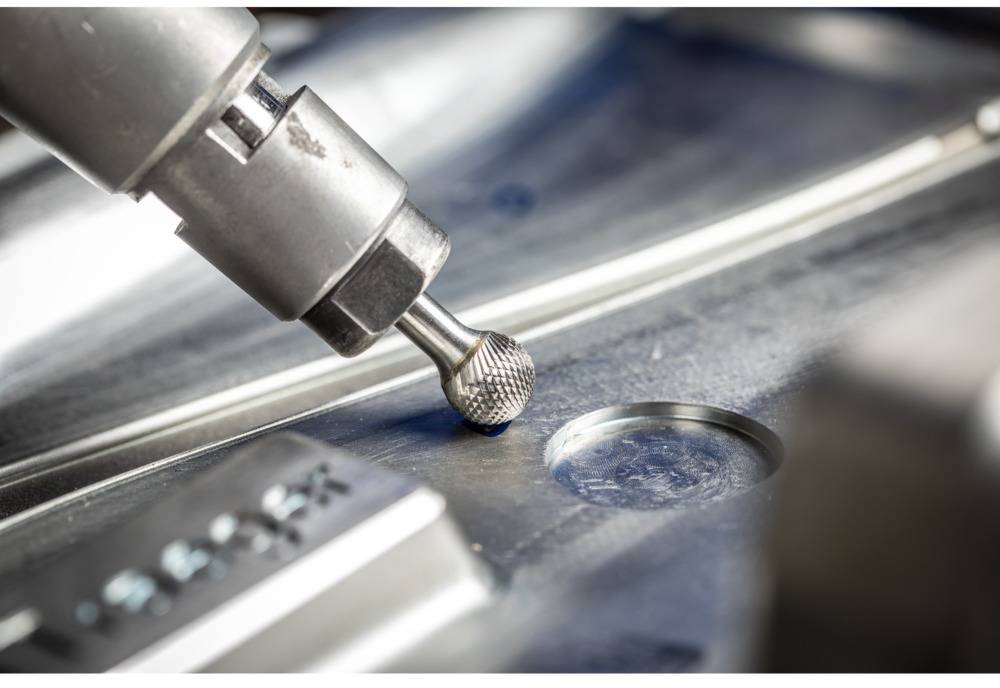 Machine drill with a round head engraving metal surface; close-up shows precision manufacturing with smooth, gleaming surface.