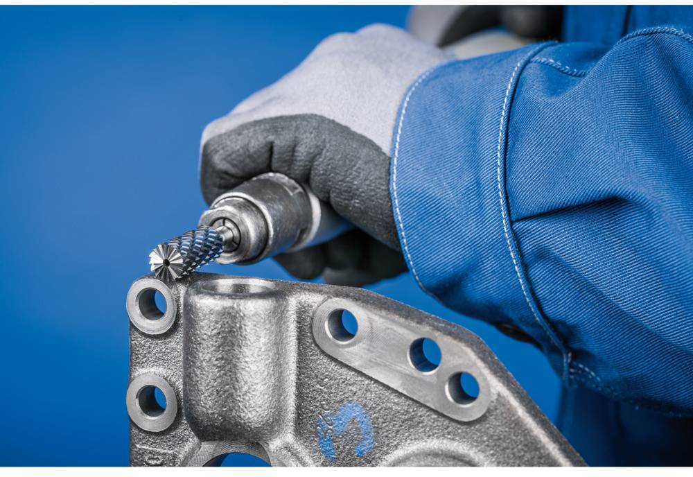 'Worker in blue protective clothing machining a metal component with a milling tool, detailed close-up of manual work.'