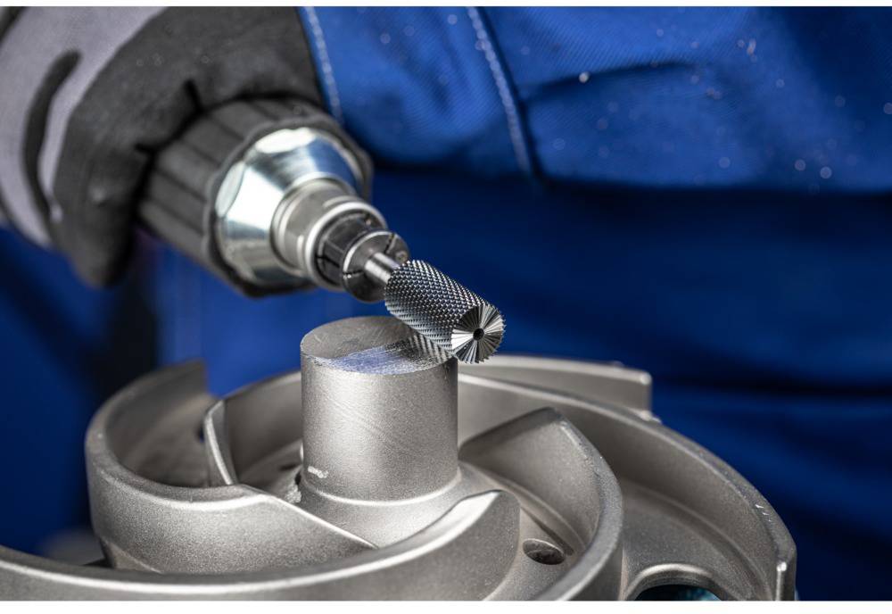 A person is grinding a metal part with an abrasive tool. The image shows a close-up of the process.