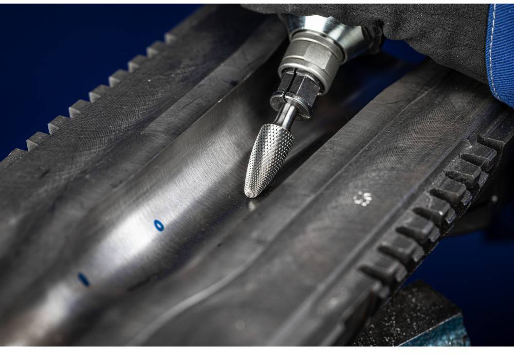 A milling machine is machining a metal surface to remove irregularities. A hand wearing a glove is holding the device.