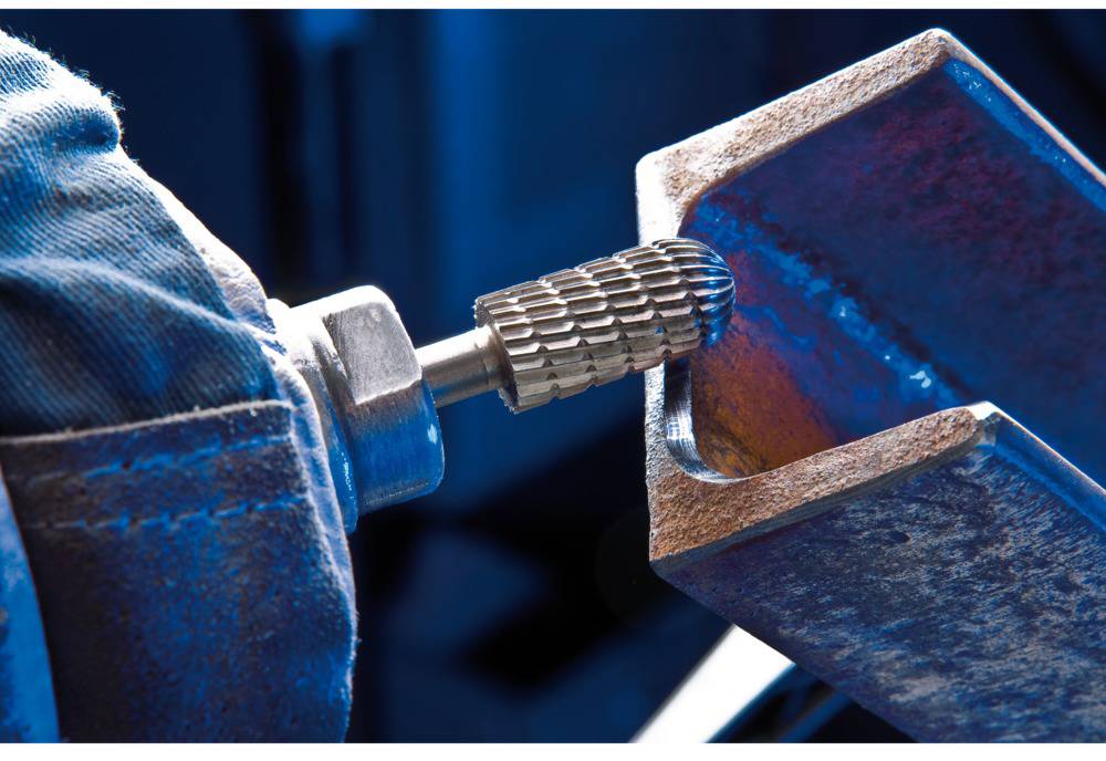 A grinding tool smooths the edge of a metal piece. A close-up reveals the texture of the rusty metal and the tool.