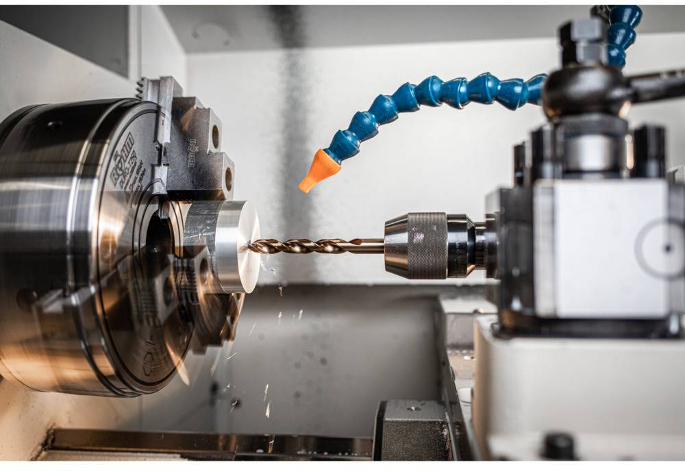 A metalworking lathe workstation shows a rotating metal block and a drill penetrating the material.