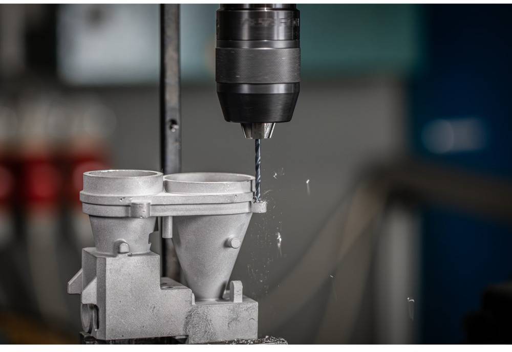 A machine is drilling precise holes in a metal component in a workshop setting, focusing on the drill bit and the machined workpiece.