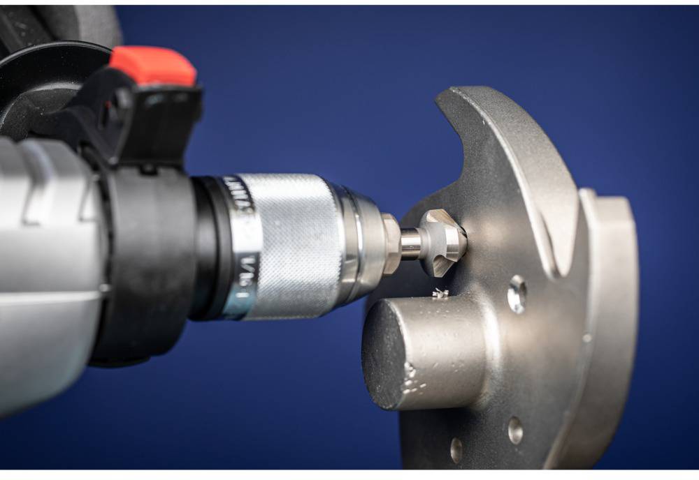 A close-up of a spanner turning a screw into a metal component. The background is a uniform blue.
