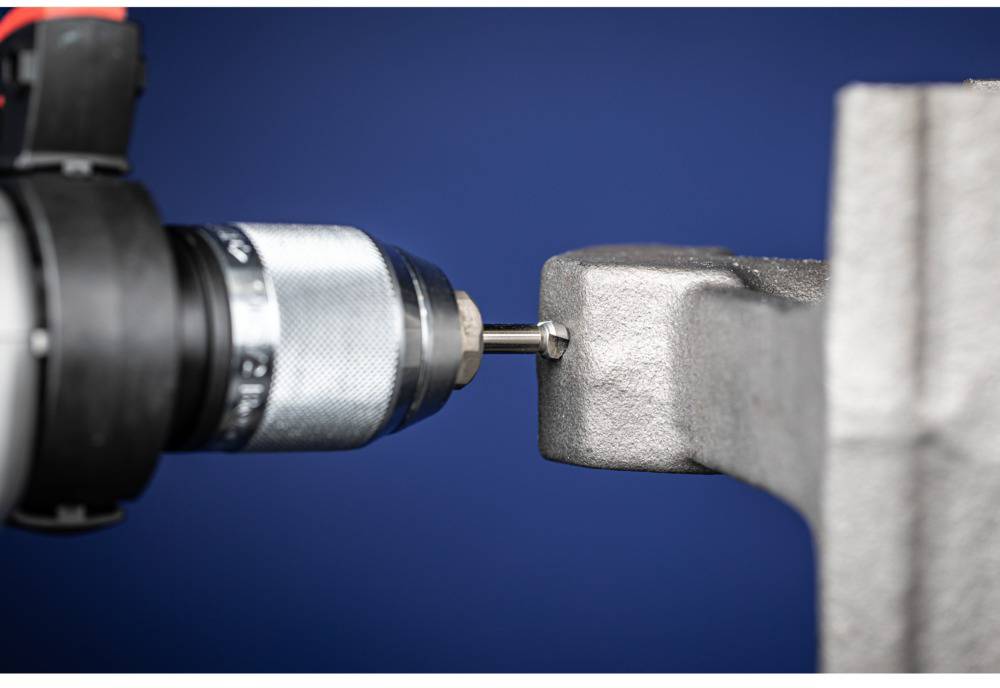 'Close-up of a drill bit drilling into metal, with a blue background.'
