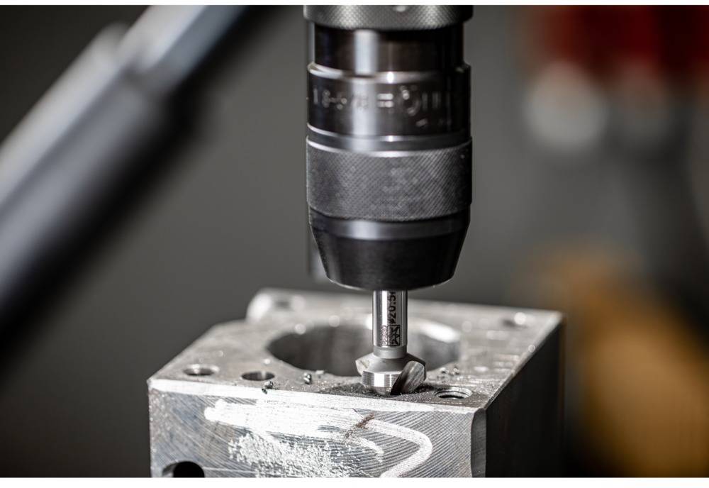 A milling machine is machining a metal plate. A rotating cutting tool is drilling precise holes.