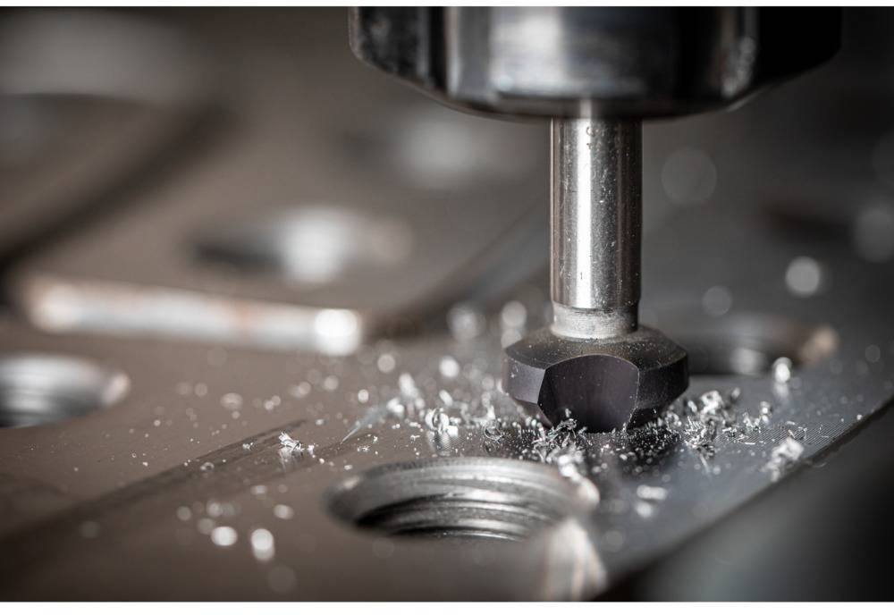 Close-up of a CNC milling machine processing metal. Sparks and metal shavings fly around the milling head. Skilled technical work in progress.