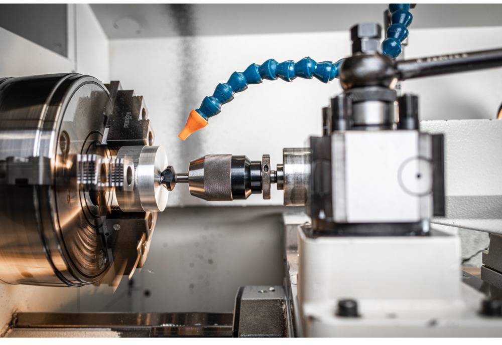 A CNC lathe is machining a metal piece. The drill is refining the surface, while a coolant hose reduces the heat.