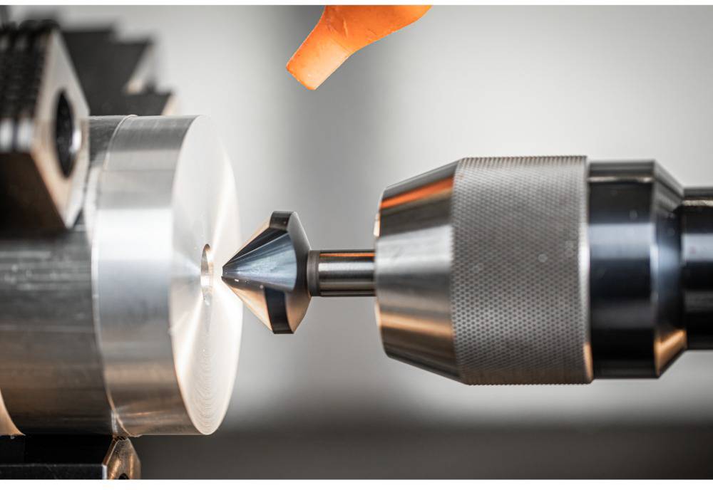 A drill is machining a circular metal piece on a lathe in a workshop, while sparks are flying.