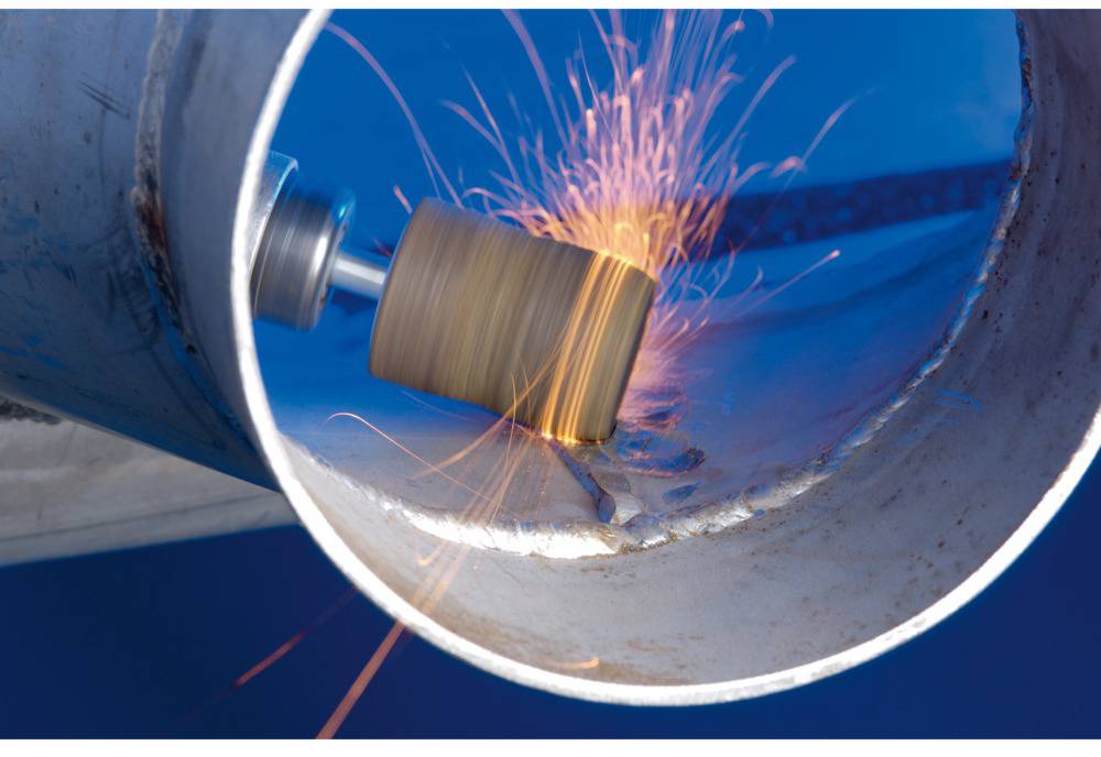 A metal pipe is being machined internally with a machine, sparks flying. The scene depicts industrial metalworking.