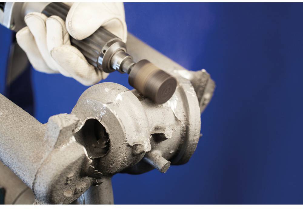 A person is using an electric grinding tool to smooth a metal surface. Protective gloves are visible.