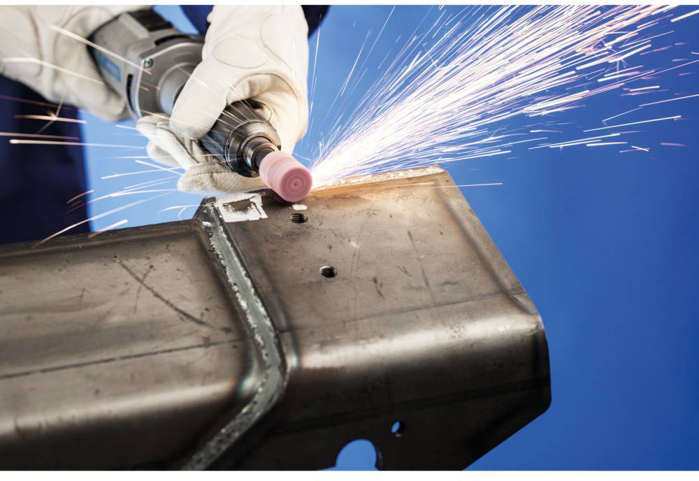 A person is grinding metal with an electric tool, sparks flying. Background in blue.