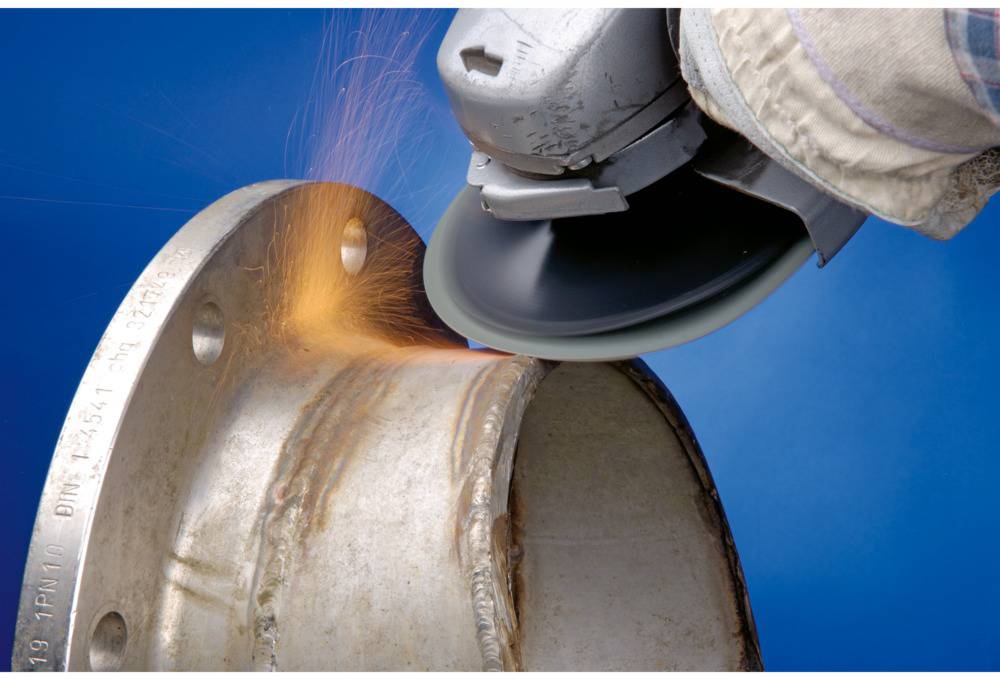 'Close-up of an angle grinder spraying sparks while working on metal. A worker is holding the grinder on a pipe connection.'