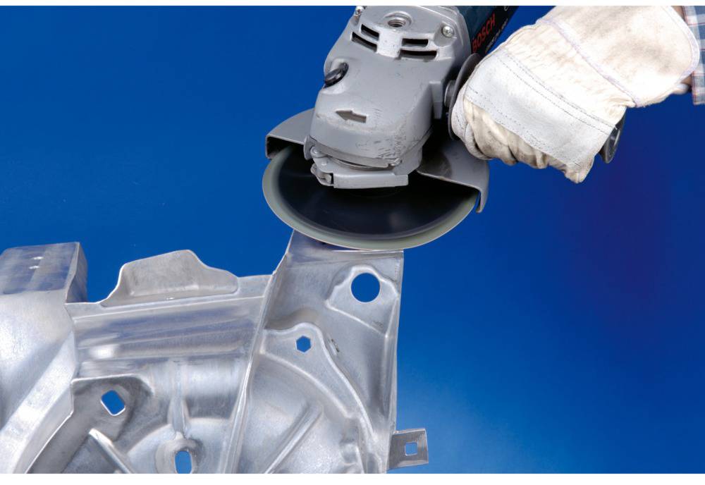 A person is grinding a metal part with an angle grinder. The person is wearing work gloves and the machine is generating sparks.