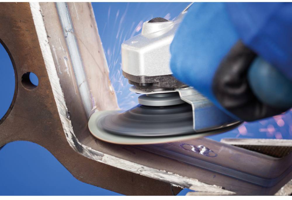 A person is grinding the edge of a metal piece with a grinding machine. Sparks are flying as the tool works.