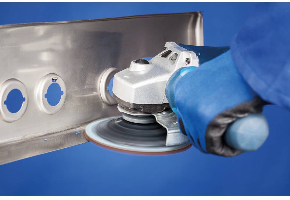 A person is using an electric grinding machine to work on a metal surface. The person is wearing blue safety gloves.