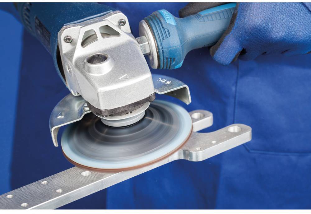 A person is using an angle grinder to grind a metal part. The rotating disc is touching the material.