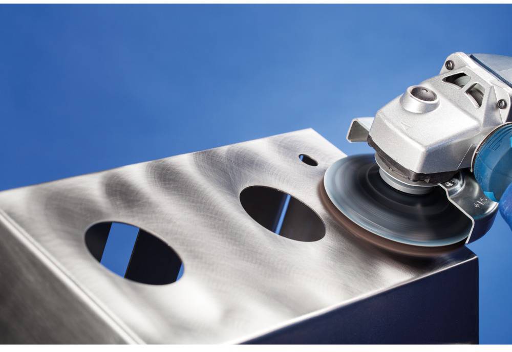 An angle grinder polishes a metal surface with circular cuts to smooth and refine it.