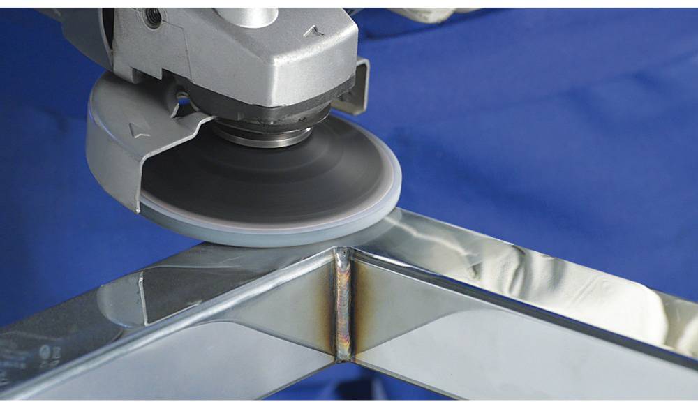 A grinding machine is machining the edge of a metal frame while it is positioned at an angle. The tool removes material to create a smooth surface.